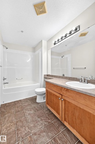 Integrated bathtub and shower combination, tiled flooring, wood-finish vanity with a single sink, large vanity mirror, and overhead strip lighting - #1303 330 Clareview Station Dr Nw, Edmonton, AB 