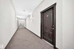 Long hallway featuring wall-mounted sconce lighting, light-toned walls, dark wood-finish door frames, and patterned carpeting - 