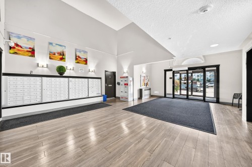 Wood-finish flooring with black carpet runner, white walls, and automatic glass entry doors - #1303 330 Clareview Station Dr Nw, Edmonton, AB 
