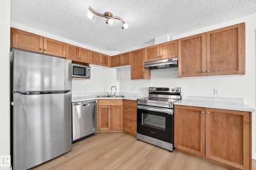 Kitchen featuring wood-finish cabinetry, stainless steel appliances, white countertops, and wood-finish flooring - #1303 330 Clareview Station Dr Nw, Edmonton, AB 