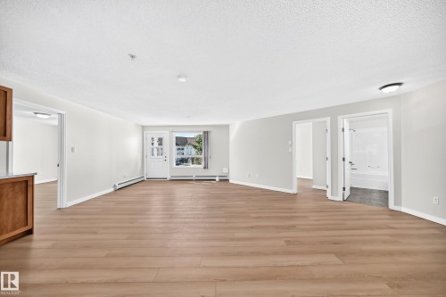 Light-toned wood-finish flooring, white painted walls, and a white entry door with glass panels - #1303 330 Clareview Station Dr Nw, Edmonton, AB 