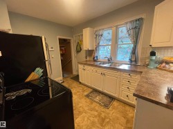 Kitchen featuring white cabinetry, a double basin stainless steel sink, a tiled backsplash, a black electric range, and solid surface countertops - 