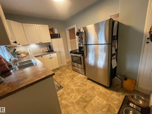 Kitchen featuring white cabinetry, stainless steel appliances, a double basin sink, and wood-finish countertops - 11230 96 Street Nw, Edmonton, AB 