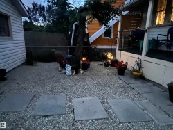 Gravel patio area with concrete pavers, featuring a mature tree and a chain-link fence - 
