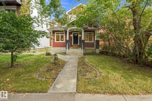 Red siding exterior with white trim, covered front porch, stone column accents, and a concrete pathway leading to the entrance - 10143 123 Street Nw, Edmonton, AB 