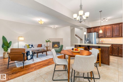 Open-concept living area with wood-finish flooring, a tiled fireplace, and a kitchen featuring wood cabinetry, stainless steel appliances, and a breakfast bar with pendant lighting - 10143 123 Street Nw, Edmonton, AB 