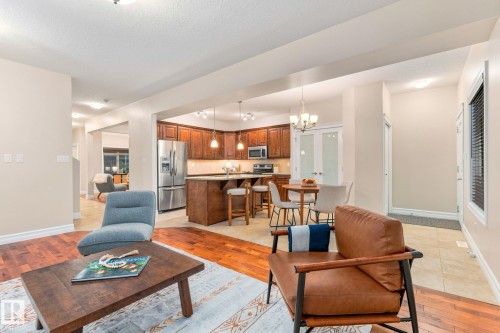 Open-concept living area with wood-finish flooring, recessed lighting, and a kitchen featuring wood cabinetry, stainless steel appliances, and a breakfast bar - 10143 123 Street Nw, Edmonton, AB 