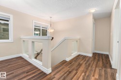 Wood-finish flooring, contemporary glass panel railing, white trim details, recessed lighting, and a decorative pendant light fixture - 