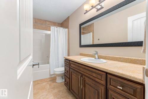 Bathroom featuring a wood-finish vanity with an integrated sink, a large framed mirror, a three-light vanity fixture, a tiled shower-tub combination, and tiled flooring - 10143 123 Street Nw, Edmonton, AB 