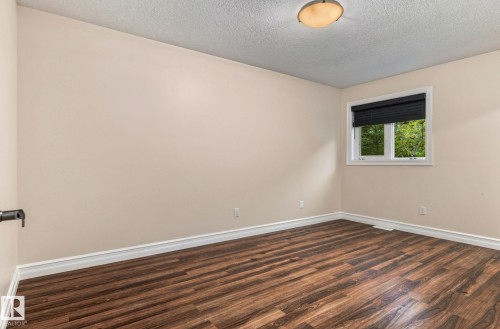 Wood-finish flooring, neutral wall paint, white trim, single window with black blinds, and a flush-mount ceiling light - 10143 123 Street Nw, Edmonton, AB 