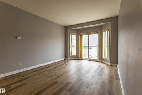 Spacious room featuring wood-finish flooring, light grey walls, and white baseboards - #412 4304 139 Av Nw, Edmonton, AB - Indoor Photo Showing Other Room