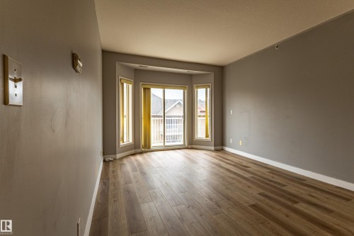 Spacious room featuring wood-finish flooring, light gray walls, and white baseboards - #412 4304 139 Av Nw, Edmonton, AB - Indoor Photo Showing Other Room