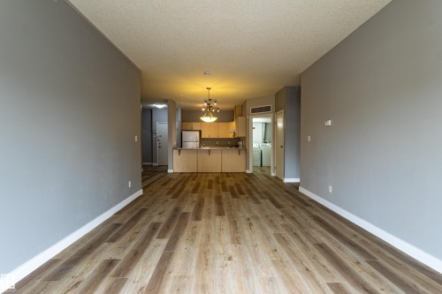 Spacious open-concept living area featuring wood-finish flooring and light gray walls - #412 4304 139 Av Nw, Edmonton, AB - Indoor Photo Showing Other Room