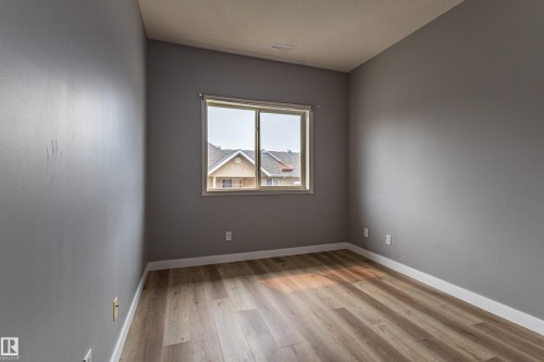 Room featuring wood-finish flooring, neutral gray walls, and white baseboards - #412 4304 139 Av Nw, Edmonton, AB - Indoor Photo Showing Other Room