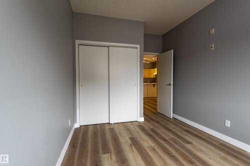 Room featuring wood-finish flooring, light grey walls, white baseboards, and a bi-fold closet door - #412 4304 139 Av Nw, Edmonton, AB - Indoor Photo Showing Other Room