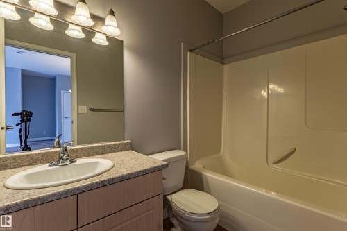 Bathroom featuring a light-toned vanity with a built-in sink, a speckled countertop, and a large mirror - #412 4304 139 Av Nw, Edmonton, AB - Indoor Photo Showing Bathroom