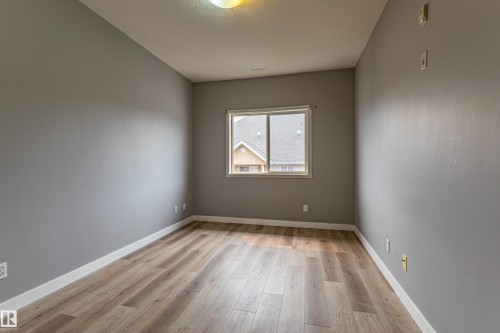 Well-lit room featuring wood-finish flooring, neutral gray walls, a white baseboard, a single window, and a ceiling-mounted light fixture - #412 4304 139 Av Nw, Edmonton, AB - Indoor Photo Showing Other Room