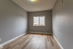 Well-lit room featuring wood-finish flooring, neutral gray walls, a white baseboard, a single window, and a ceiling-mounted light fixture - 