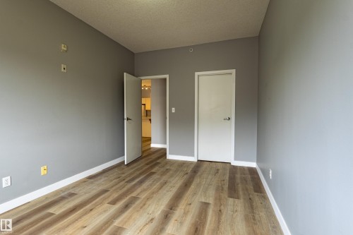 Spacious room featuring wood-finish flooring, light grey walls, white baseboards, and two white doors with dark hardware - #412 4304 139 Av Nw, Edmonton, AB - Indoor Photo Showing Other Room