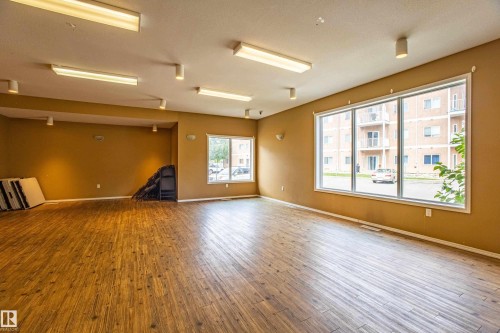 Expansive room featuring wood-finish flooring, ample natural light from multiple windows, and a combination of recessed and fluorescent ceiling lighting - #412 4304 139 Av Nw, Edmonton, AB - Indoor Photo Showing Other Room