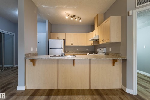 Kitchen featuring light wood-finish cabinetry, granite-style countertops, stainless steel sink, and white appliances - #412 4304 139 Av Nw, Edmonton, AB - Indoor Photo Showing Kitchen
