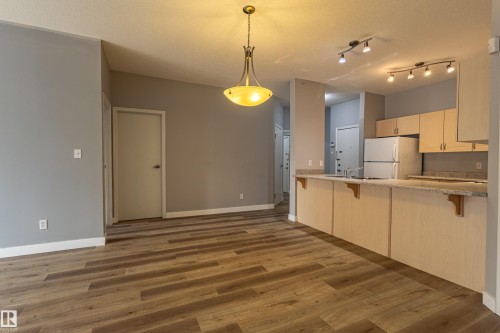 Open-concept living area featuring wood-finish flooring, a contemporary chandelier, and a breakfast bar with a stone-finish countertop - #412 4304 139 Av Nw, Edmonton, AB - Indoor Photo Showing Kitchen