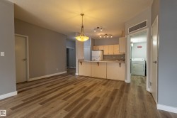Open concept living space featuring wood-finish flooring, a kitchen with light wood cabinetry and track lighting, and a separate laundry area with a washer and dryer unit - 
