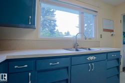 Kitchen featuring a double basin stainless steel sink, gooseneck faucet, and blue cabinetry with white hardware - 