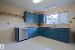 Kitchen featuring blue cabinetry, light-toned countertops, a stainless steel dishwasher, a window over the sink, and track lighting - 