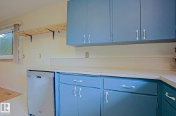 Light blue cabinetry with white hardware, solid surface countertops, and a stainless steel dishwasher - 