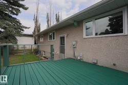 Outdoor wooden deck with painted green surface and railing, stucco exterior, and white-framed windows - 