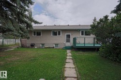 Expansive lawn with a paver pathway, mature trees, and a raised wooden deck with railings - 