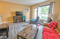 Living area featuring wood-finish flooring, warm-toned walls, a large window, and a glass-paneled door - 