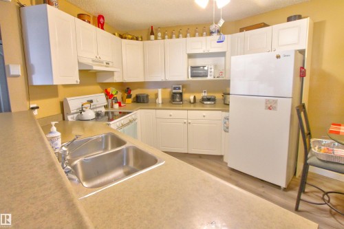 Kitchen featuring white cabinetry, a double basin stainless steel sink, light-toned countertops, and wood-finish flooring - #106 2 Alpine Bv, St. Albert, AB - Indoor Photo Showing Kitchen With Double Sink