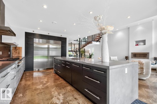 Gourmet kitchen with stainless steel appliances, dark wood-finish cabinetry, a large center island, and industrial-style flooring - 14A Birch Drive, St. Albert, AB 