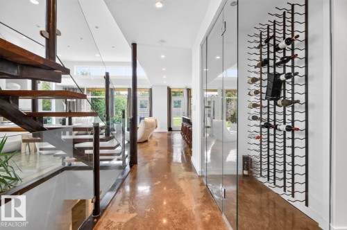 Open-tread staircase with glass railing, recessed ceiling lighting, full-height glass paneling, and a wall-mounted wine rack - 14A Birch Drive, St. Albert, AB 