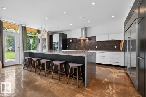 Expansive kitchen with a waterfall island, integrated cooktop, stainless steel appliances, and a mosaic tile backsplash - 14A Birch Drive, St. Albert, AB 