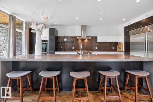 Kitchen featuring an expansive island with seating, stainless steel appliances, dark wood-finish cabinetry, a textured backsplash, and recessed lighting - 14A Birch Drive, St. Albert, AB 