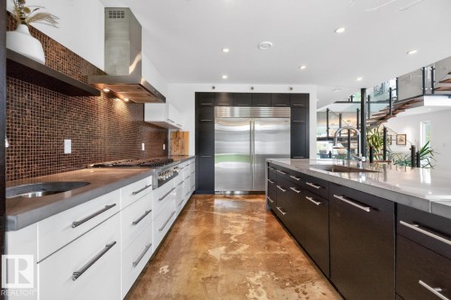 Modern kitchen featuring stainless steel appliances, a large center island with an integrated sink, custom cabinetry, and a mosaic tile backsplash - 14A Birch Drive, St. Albert, AB 