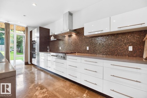 White cabinetry with integrated stainless steel appliances, a mosaic tile backsplash, and polished concrete flooring - 14A Birch Drive, St. Albert, AB 