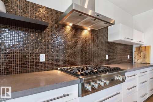 Stainless steel range with a ventilation hood, mosaic tile backsplash, white flat-panel cabinetry, and a floating shelf - 14A Birch Drive, St. Albert, AB 