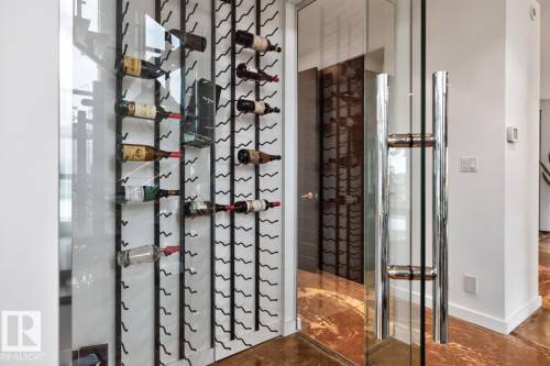 Glass-enclosed wine display with contemporary metal racking, a full-height glass door, and polished chrome hardware - 14A Birch Drive, St. Albert, AB 