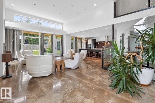 Expansive living area with high ceilings, polished concrete flooring, large glass paneling, and an open-concept kitchen with a breakfast bar - 14A Birch Drive, St. Albert, AB 