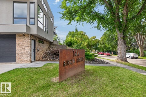 Modern architectural design featuring expansive windows, natural stone facade, and a dark-toned garage door - 14A Birch Drive, St. Albert, AB 