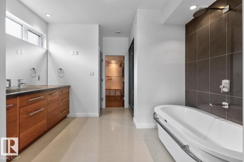 Dual vanity with wood-finish cabinetry, built-in soaking tub, rain shower head, and large format wall tile - 14A Birch Drive, St. Albert, AB 