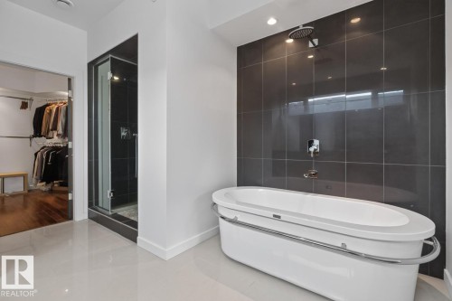 Freestanding soaking tub with chrome accents, dark large-format tile shower wall, glass-enclosed shower, walk-in closet with built-in organization, and light-colored floor tiles - 14A Birch Drive, St. Albert, AB 