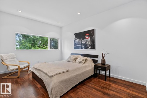 Recessed ceiling lighting, a wide horizontal window, wood-finish flooring, and a dark wood bed frame - 14A Birch Drive, St. Albert, AB 