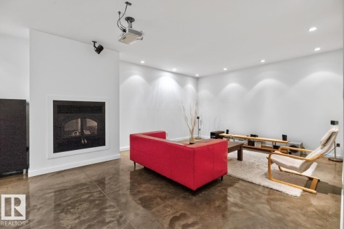 Integrated fireplace with a white mantel, ceiling-mounted projector, recessed lighting, track lighting, and polished concrete flooring - 14A Birch Drive, St. Albert, AB 