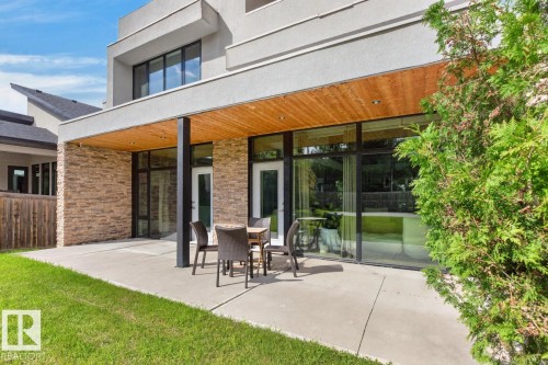 Outdoor patio with a wood-finish ceiling, stone veneer accent wall, and expansive glass doors - 14A Birch Drive, St. Albert, AB 