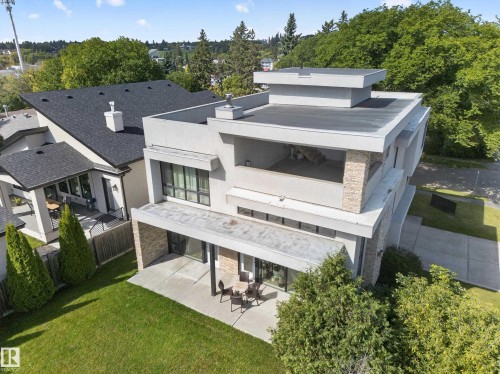 Contemporary architecture featuring a flat roofline, stone accents, multiple outdoor patios, a private balcony, and a manicured lawn - 14A Birch Drive, St. Albert, AB 